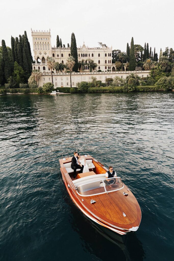 Cinematic moment of the couple on a classic wooden Riva-style boat approaching Isola del Garda