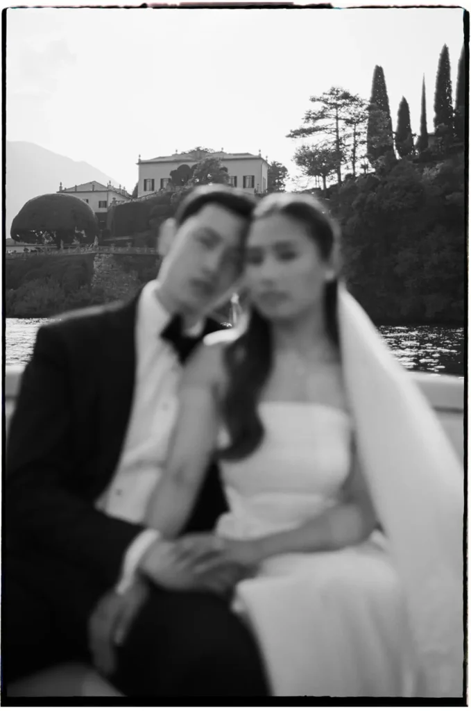 Black-and-white film-style portrait of an eloping couple on a Lake Como boat near Villa del Balbianello.