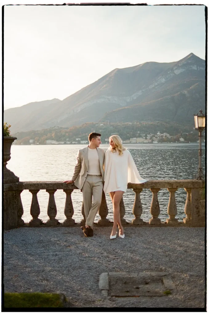 Couple standing by the lakeside balustrade at Grand Hotel Villa Serbelloni Bellagio with Lake Como and mountains at sunset