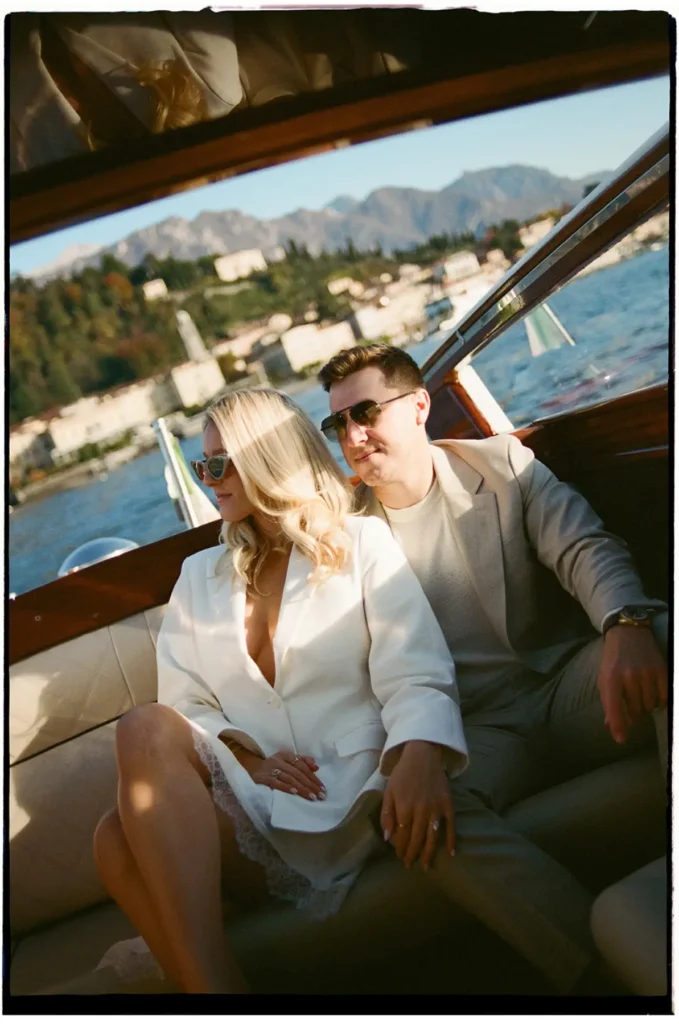 Couple relaxing on a classic wooden boat on Lake Como near Bellagio, elegant engagement portrait with mountains in the background