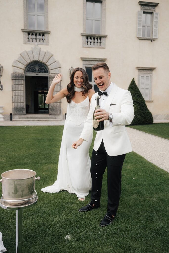 Couple opening champagne on the lawn at Villa Balbiano after their vows